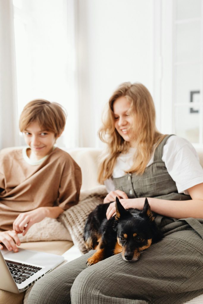 Two siblings relaxing on a sofa with their dog, enjoying quality time together indoors.